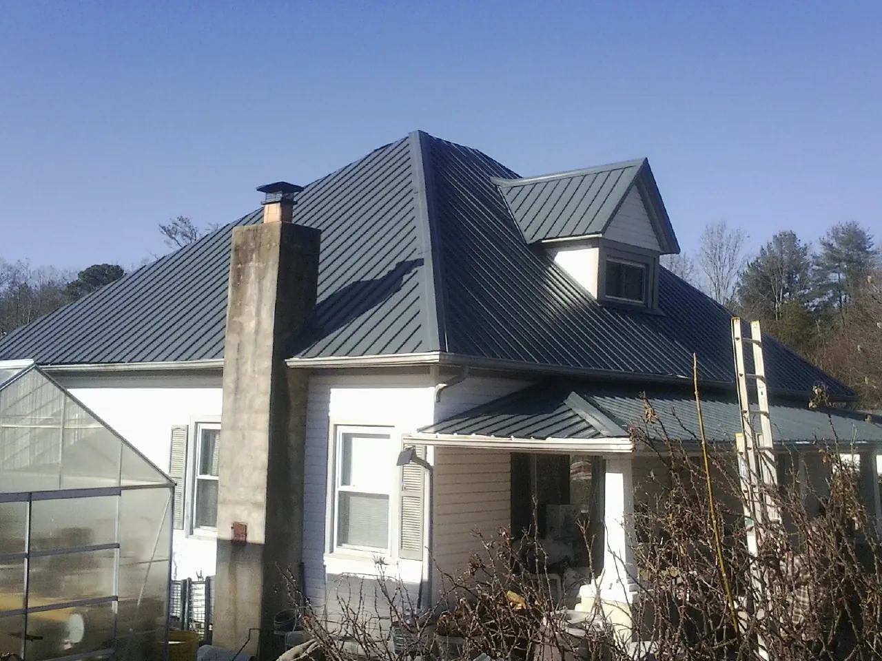 Dark blue standing seam metal roof on a white farmhouse with dormer — Slate & Tile Roof Repair by Roofing Brothers in Victor