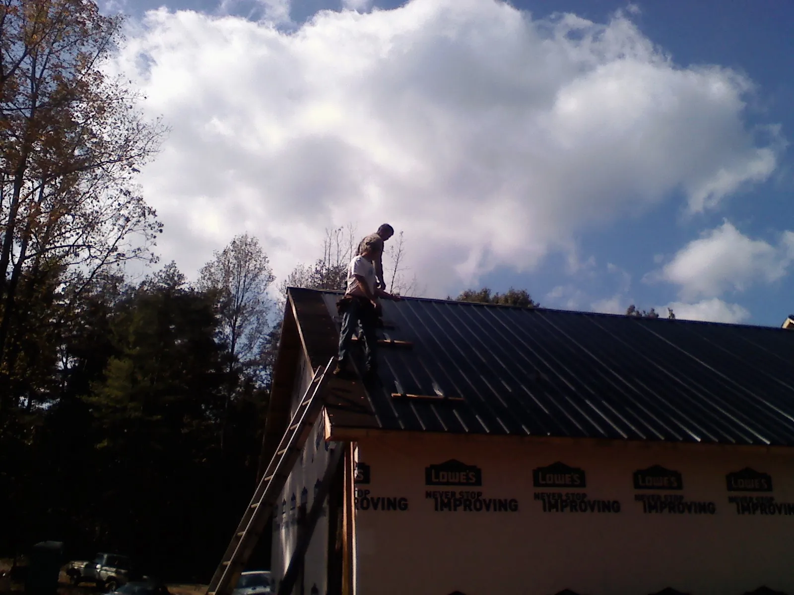 Roofer fastening dark metal panels high against a cloudy sky, from a Roof Inspection job in Victor
